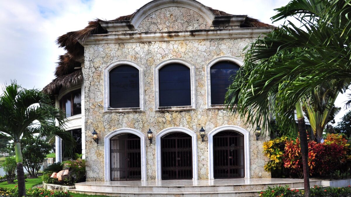 A historic stone building with arched windows surrounded by tropical foliage.