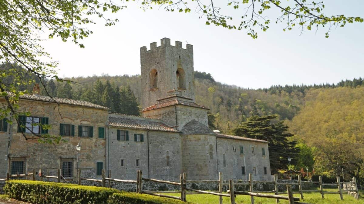 An ancient stone building with a tower, nestled in a lush green landscape with a backdrop of forested hills.