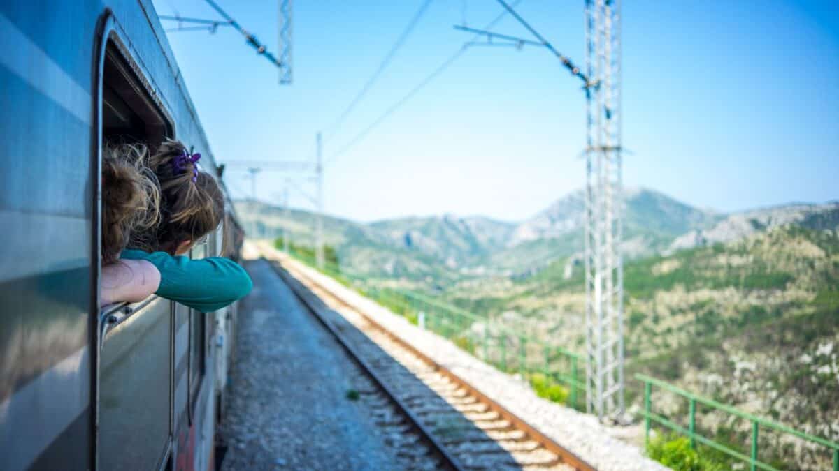 A child leans out of a train window, gazing at the scenic mountain landscape.