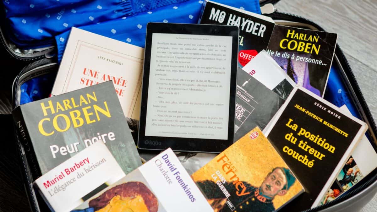 An open suitcase filled with various mystery and thriller novels in french and an e-reader displaying text on top of the books.