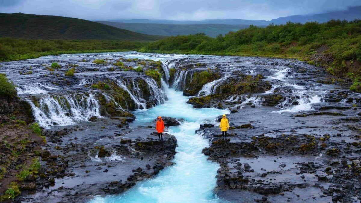Two people in bright orange and yellow jackets stand by the Br&uacute;arfoss waterfall in Iceland.