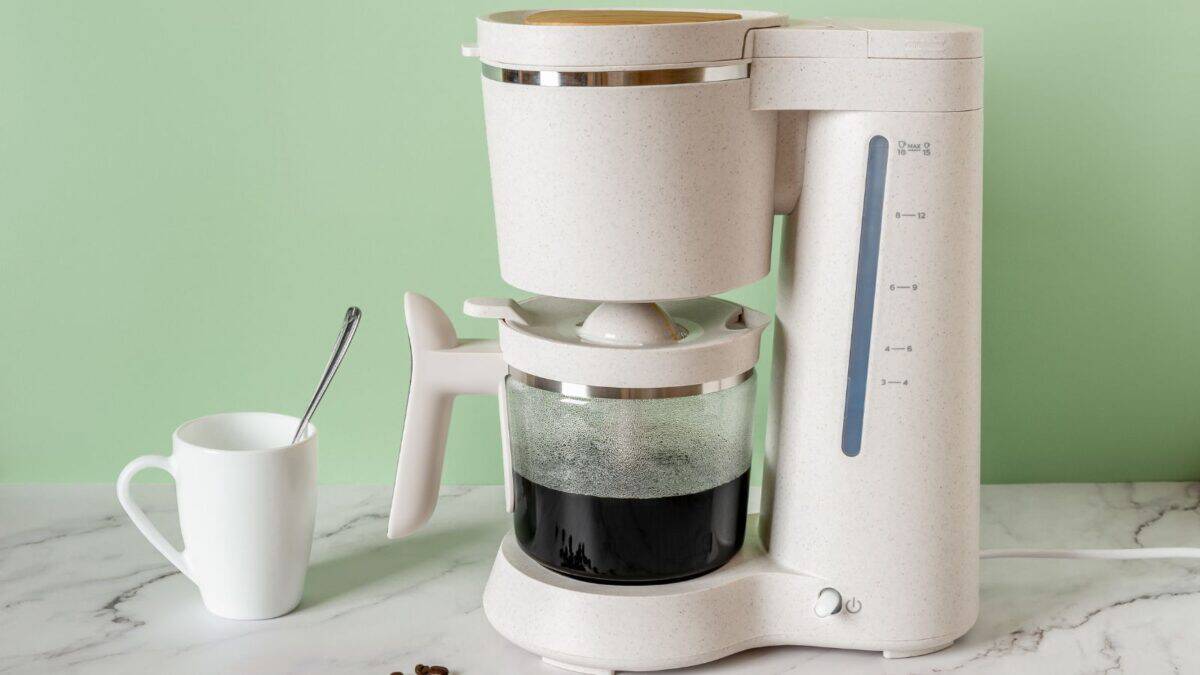 20 Ultimate No-Nos of Cruise Packing—Learn What's Banned 7 A contemporary white coffee maker with a speckled design, brewing coffee into a glass carafe, next to a white mug and a spoon on a light green countertop.