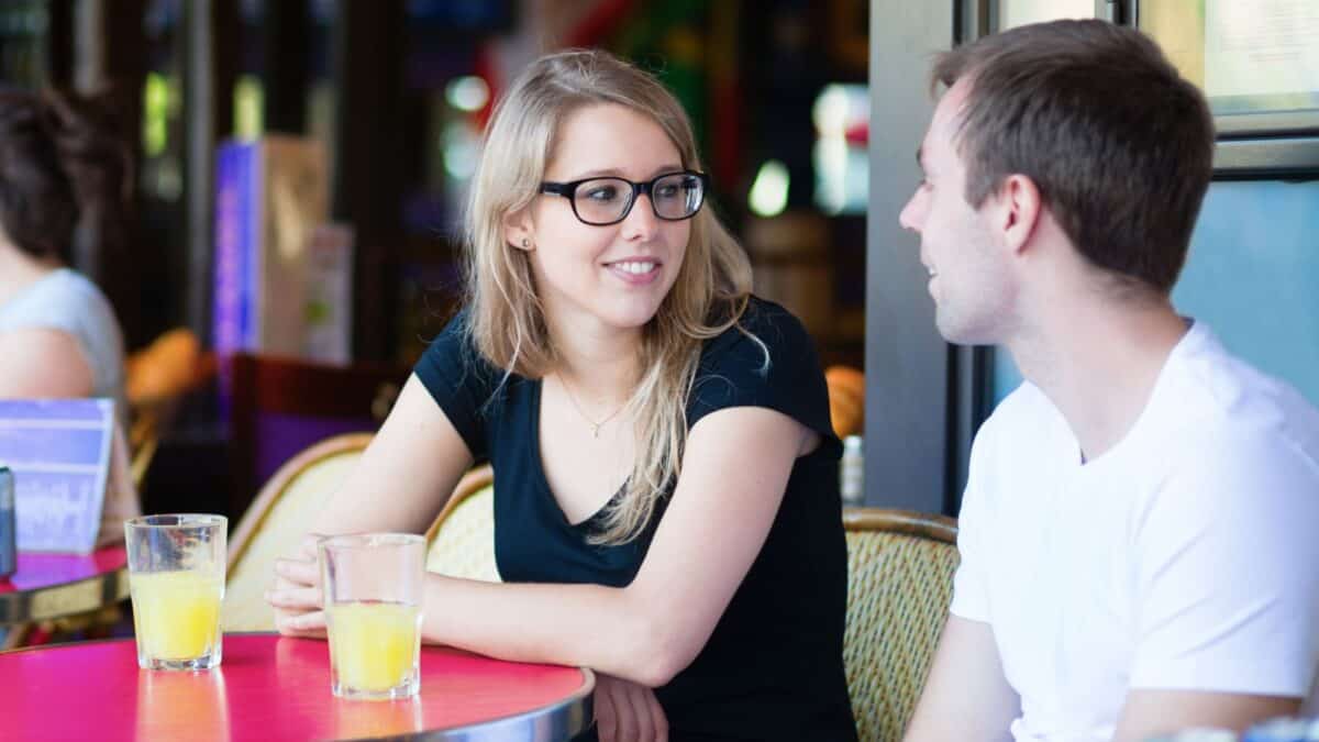 A woman wearing glasses and a man talking outside the cafe.