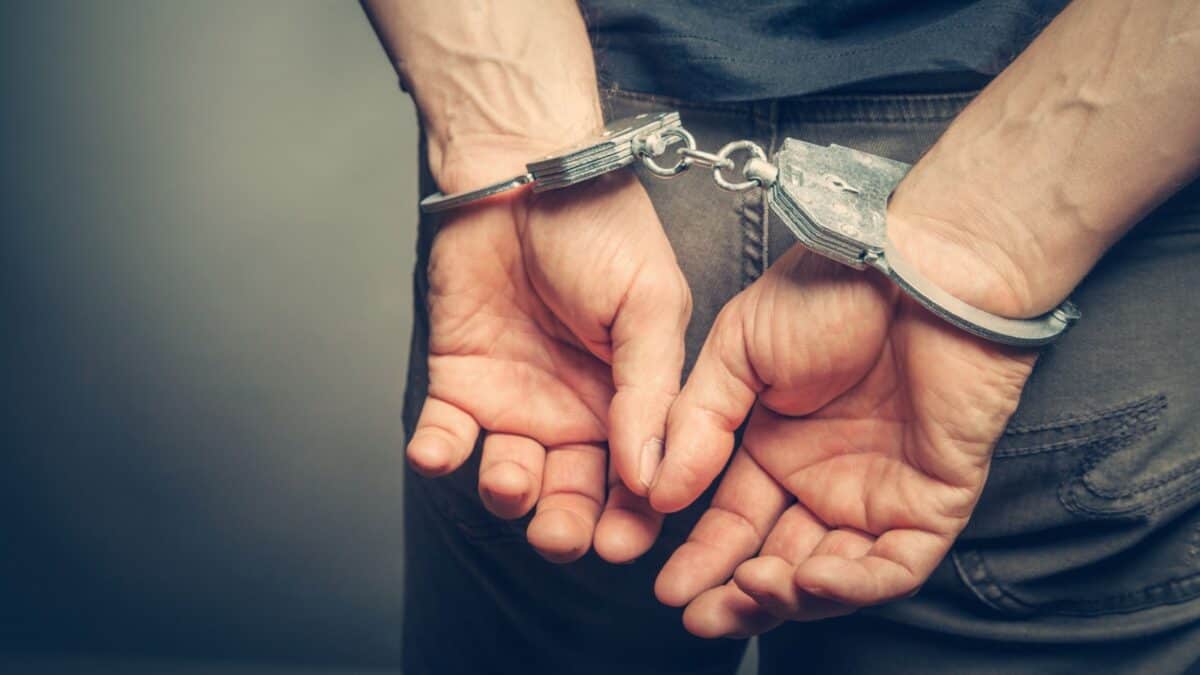 20 Ultimate No-Nos of Cruise Packing—Learn What's Banned 15 Close-up of a person's hands handcuffed behind their back, set against a muted grey background, suggesting arrest or confinement.