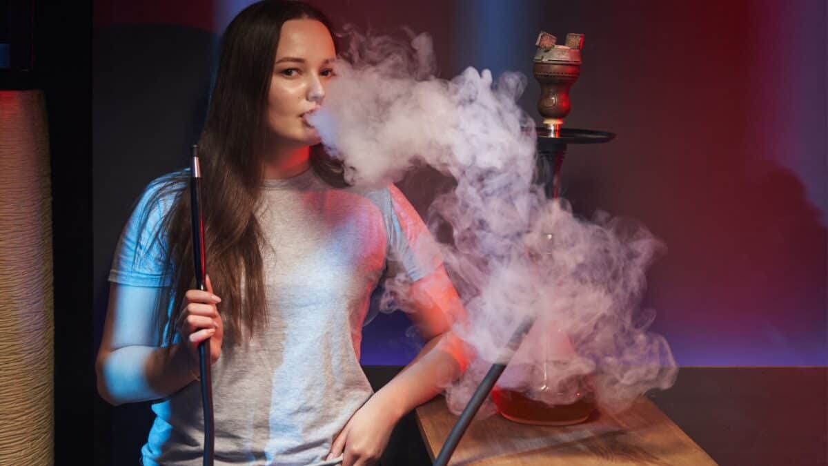 20 Ultimate No-Nos of Cruise Packing—Learn What's Banned 21 A young woman exhales a large cloud of smoke while holding a hookah hose in a dimly lit room with a red ambiance. a hookah is visible on the table beside her.