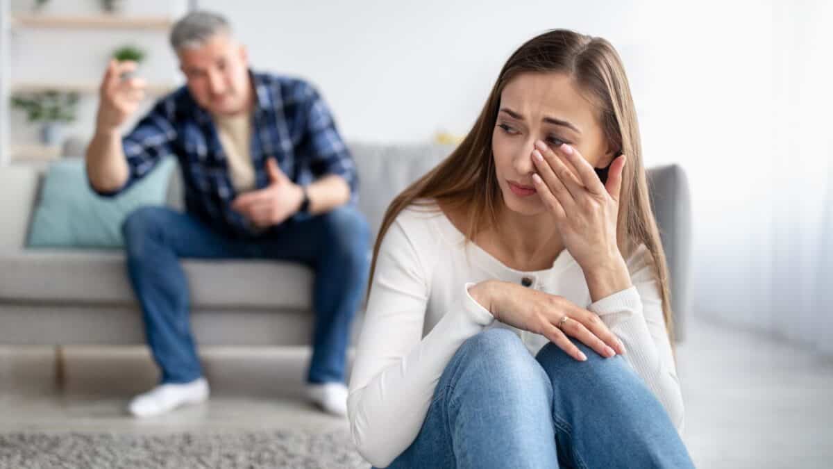 Inside the Narcissist's Playbook: 20 Tactics to Control and Confuse 4 A distressed young woman sitting with her hand on her face while an older man gestures empathetically in the background in a bright living room.