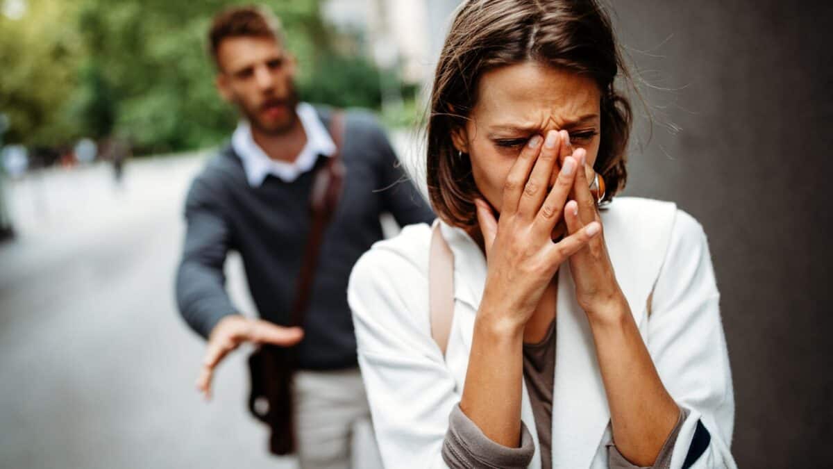 Inside the Narcissist's Playbook: 20 Tactics to Control and Confuse 17 A distressed woman covers her face with her hands on a city street, while a concerned man approaches from behind, trying to comfort her.