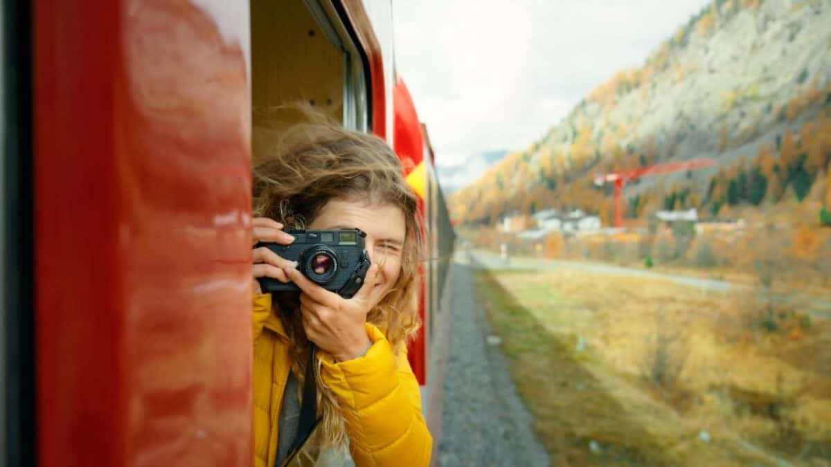 A person taking photos out of a train window, capturing the autumn-colored landscape.