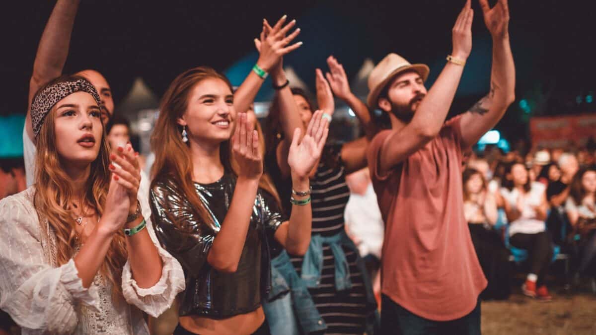 A group of enthusiastic young adults clapping and enjoying a performance at an outdoor music festival at night.