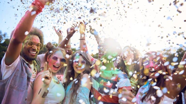 A group of joyful young friends throwing confetti and celebrating outdoors on a sunny day, expressing happiness and friendship. they are wearing colorful summer clothes and sunglasses.
