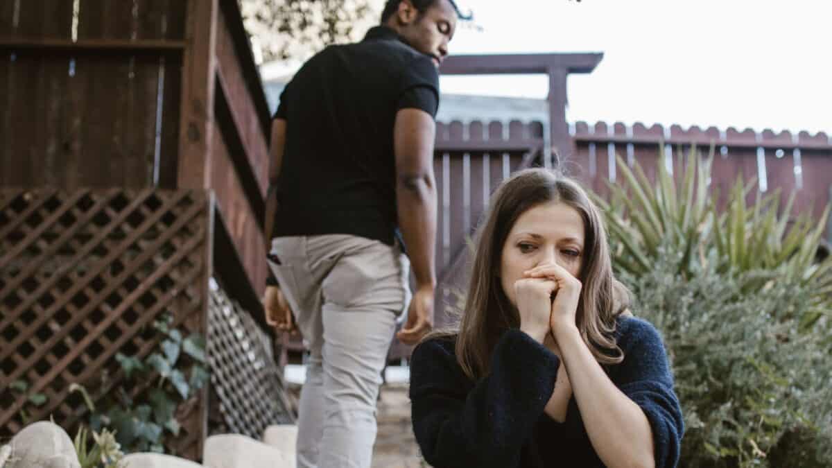 Inside the Narcissist's Playbook: 20 Tactics to Control and Confuse 11 A woman sits on outdoor steps looking distressed, covering her mouth with her hands, while a man walks away in the background.