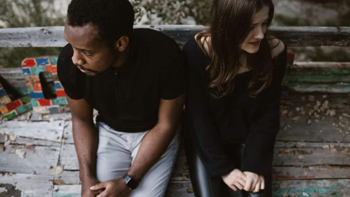 Inside the Narcissist's Playbook: 20 Tactics to Control and Confuse 13 A man and a woman sit apart on a colorful, weathered bench, surrounded by natural scenery, looking thoughtful and distanced from each other.