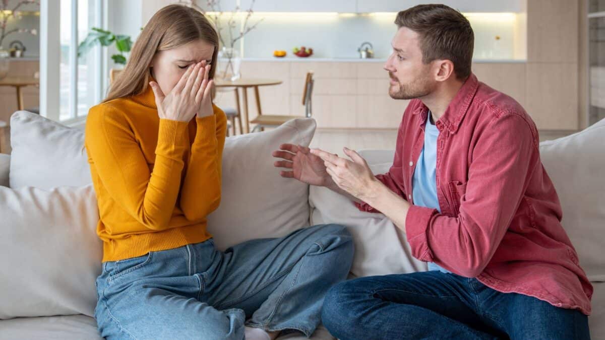 Inside the Narcissist's Playbook: 20 Tactics to Control and Confuse 3 A man and a woman sit on a sofa. the woman, in a yellow top, covers her face with her hands, seemingly upset. the man, in a red shirt, gestures while speaking to her, his expression concerned.
