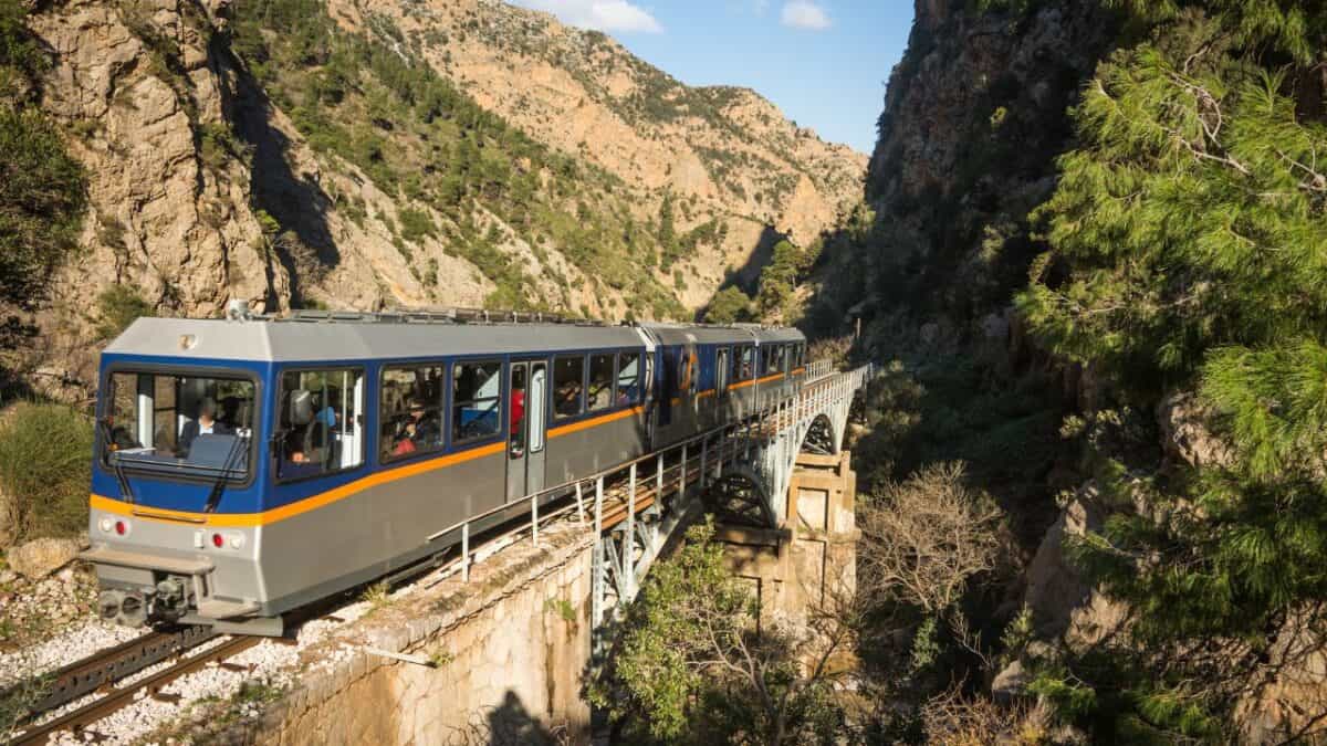 A train crossing a bridge in a mountainous terrain with dense foliage.