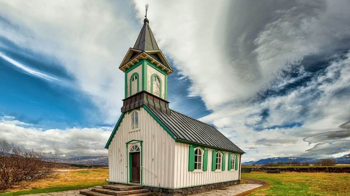 A traditional Icelandic church with a green roof and white walls under a dramatic sky.