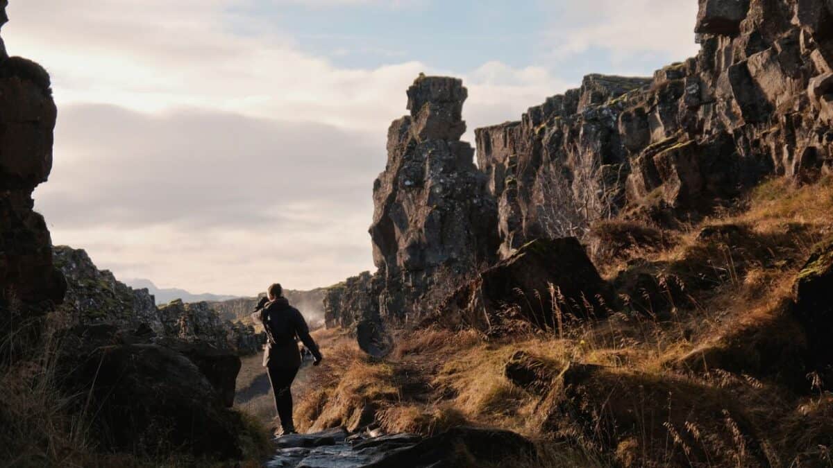 A person in a wetsuit walks through a rocky, grass-covered rift valley.