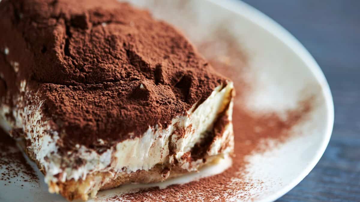 20 Phrases You Should Learn Before You Visit Italy 21 A slice of classic tiramisu dusted with cocoa powder, served on a white plate, highlighting its creamy layers and espresso-soaked ladyfingers.