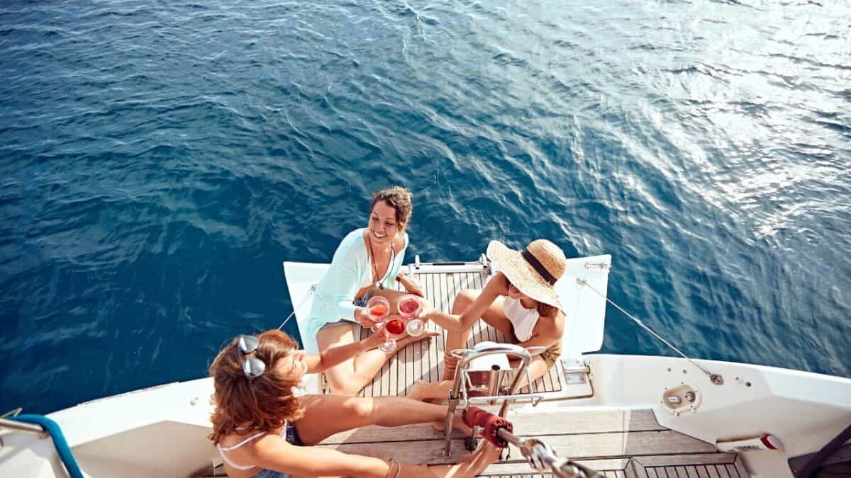 Three people enjoy drinks and each other's company on the stern of a boat, with the ocean's vast expanse in the background.