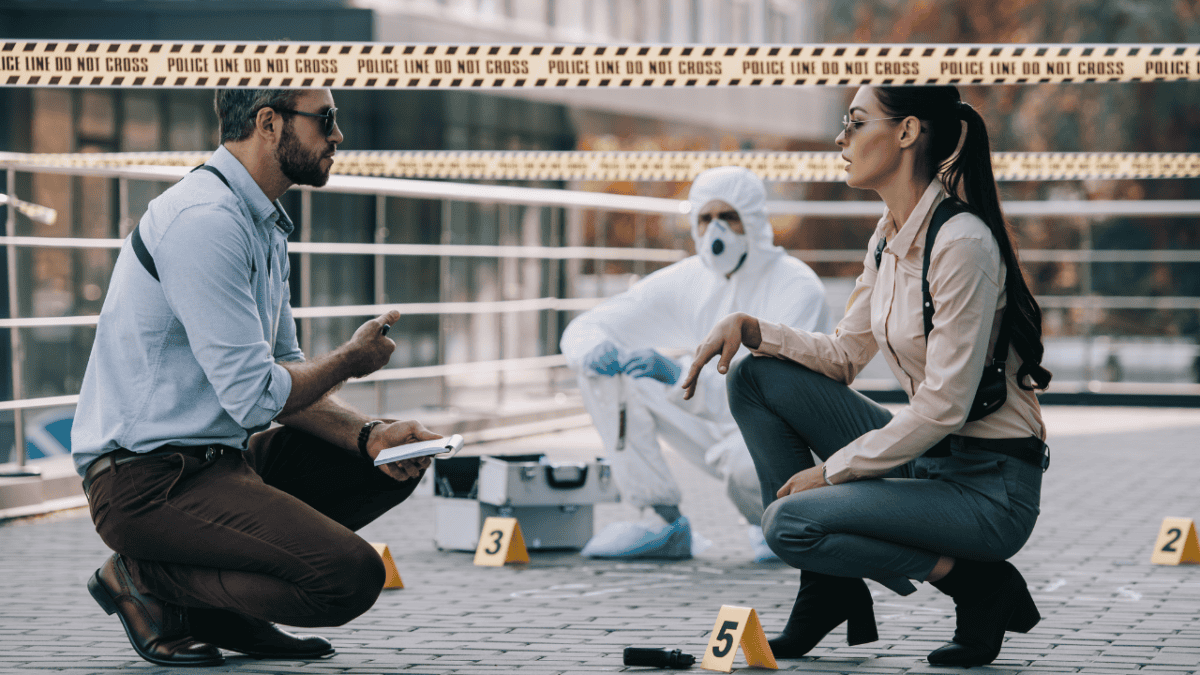 Crime scene investigation with two detectives discussing evidence, while a forensic investigator in protective gear examines the scene behind police tape."