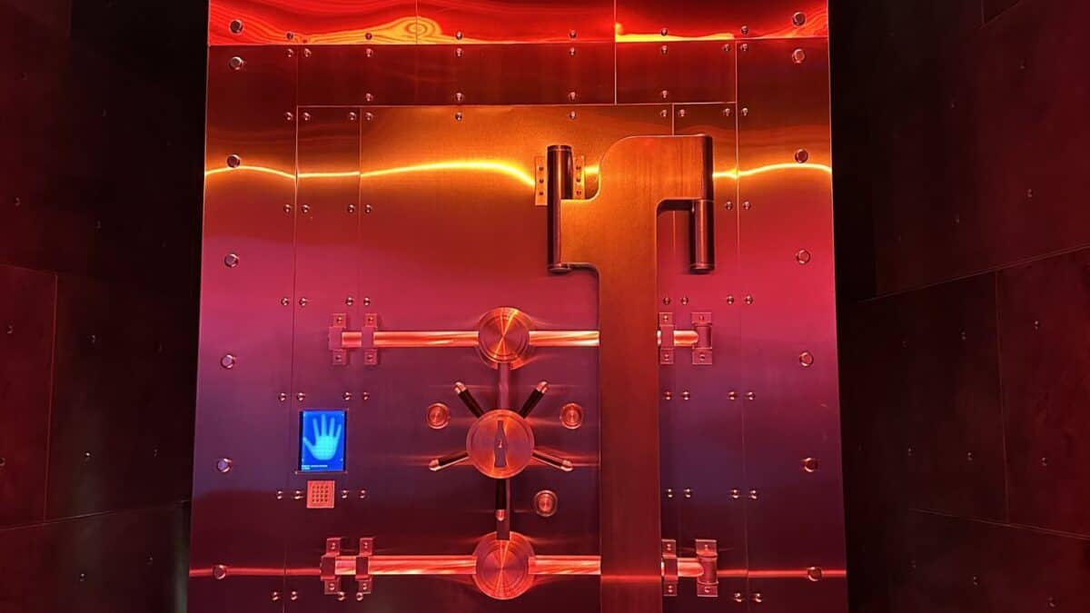 An image of a futuristic elevator interior with a vibrant red and orange color scheme, featuring glossy reflective surfaces and a prominent central panel with multiple buttons and a handprint scanner.