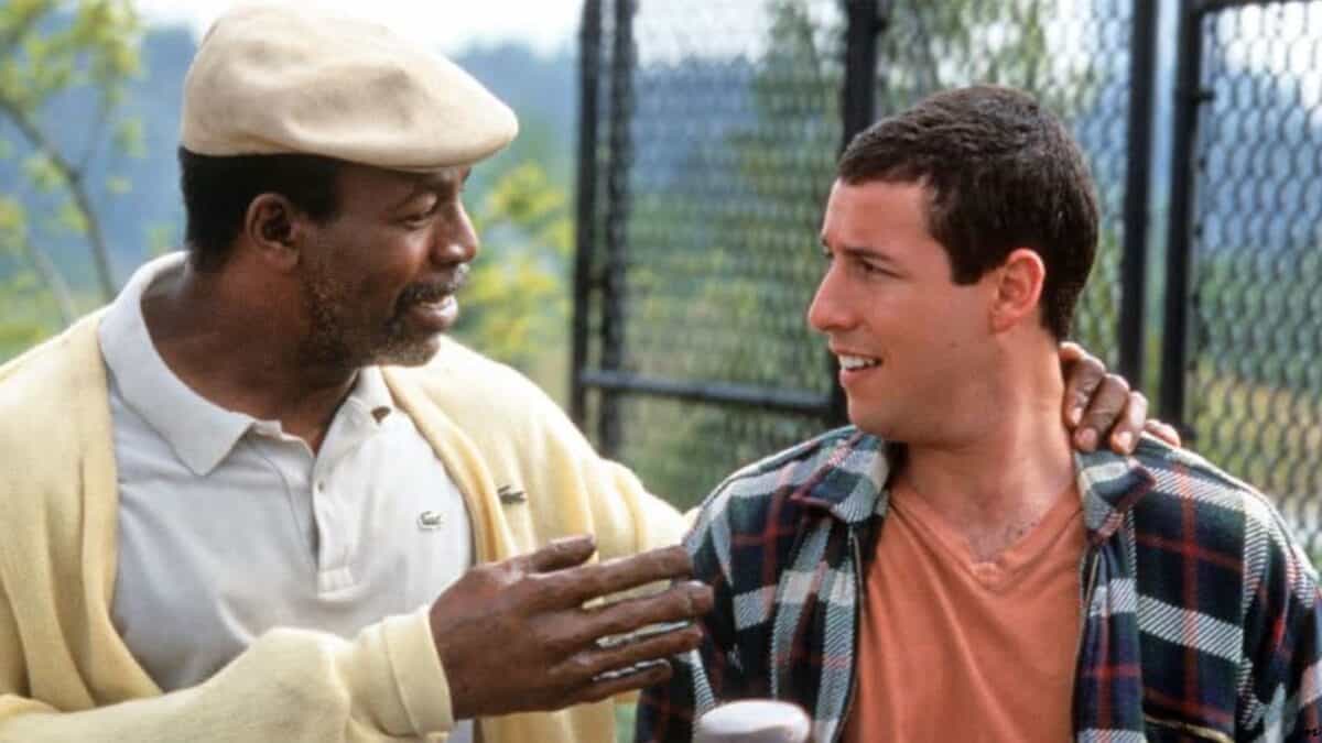 Two men in a casual outdoor setting, one African American in a cap and sweater, the other Caucasian in a plaid shirt, smiling and engaging in a friendly conversation.