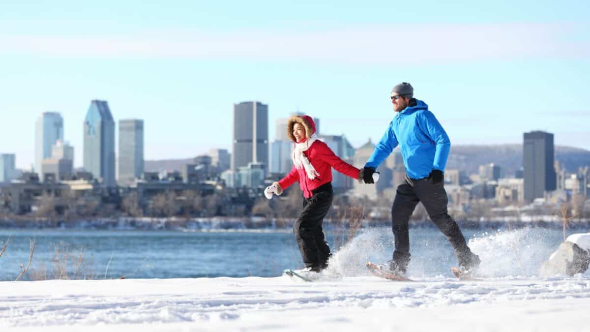 17 Friendliest Cities In The World 6 A man and woman joyfully skating on a snowy path with a city skyline in the background on a clear day.