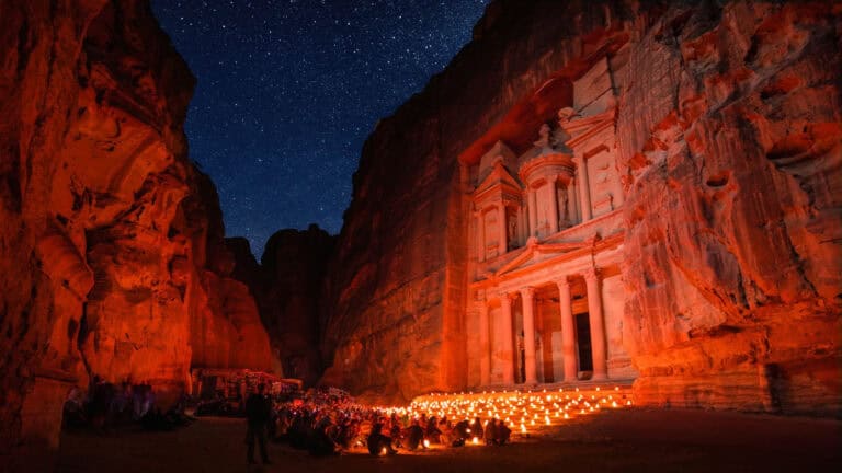 Nighttime view of the Treasury at Petra, Jordan, illuminated by candlelight with a starry sky in the background.