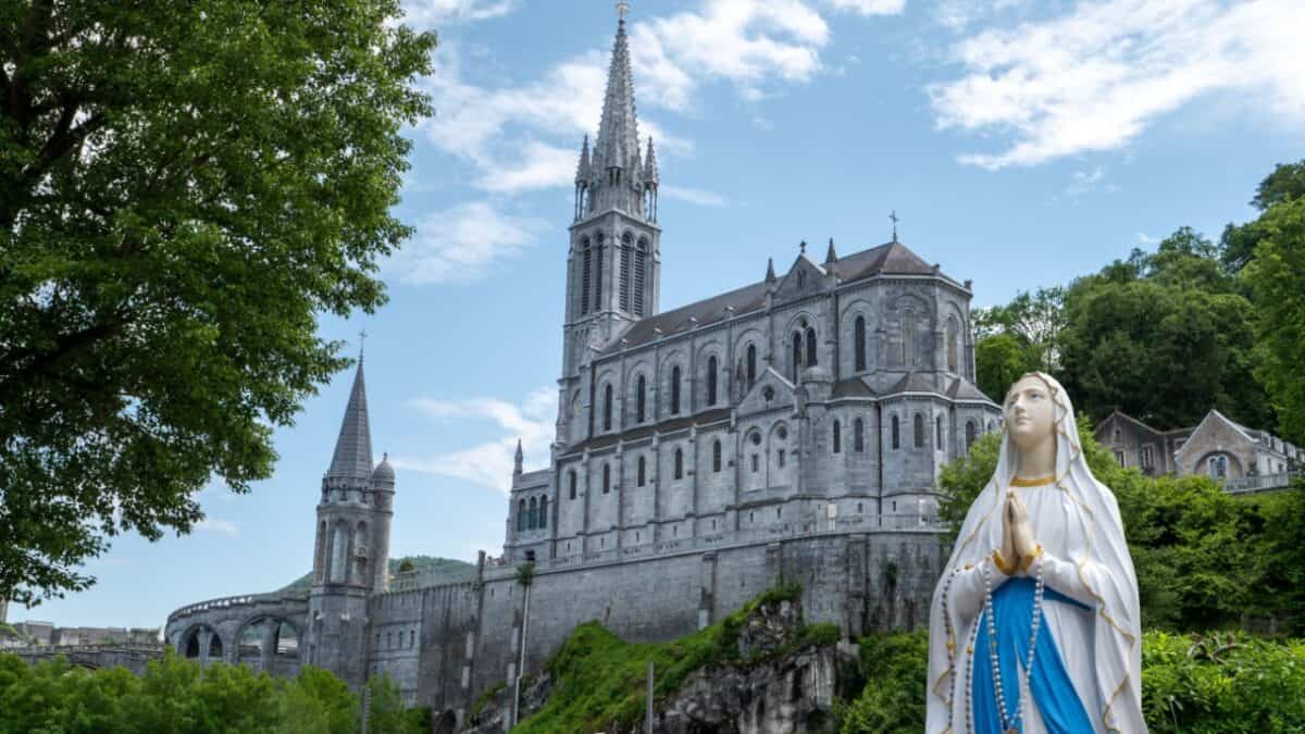 Statue of the Virgin Mary with the Basilica of Our Lady of the Rosary in Lourdes, France in the background.