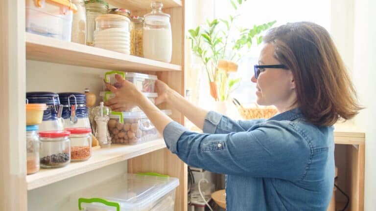 A woman organizing various jars and containers on wooden shelves in a pantry.