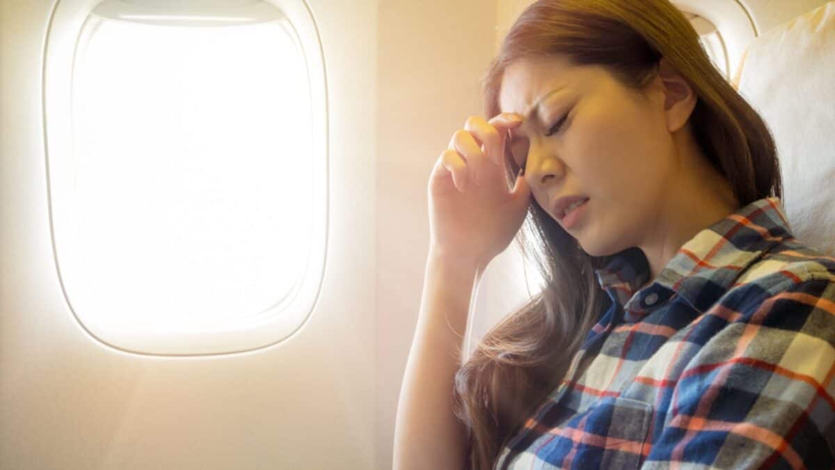 A woman on an airplane looking upset, resting her hand on her forehead while sitting by a window.