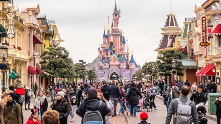 Crowded Main Street in Disneyland with people walking and the Sleeping Beauty Castle in the background.