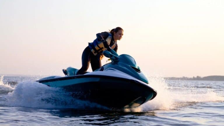 A person riding a jet ski over the water, making a splash, with a distant shoreline in the background.