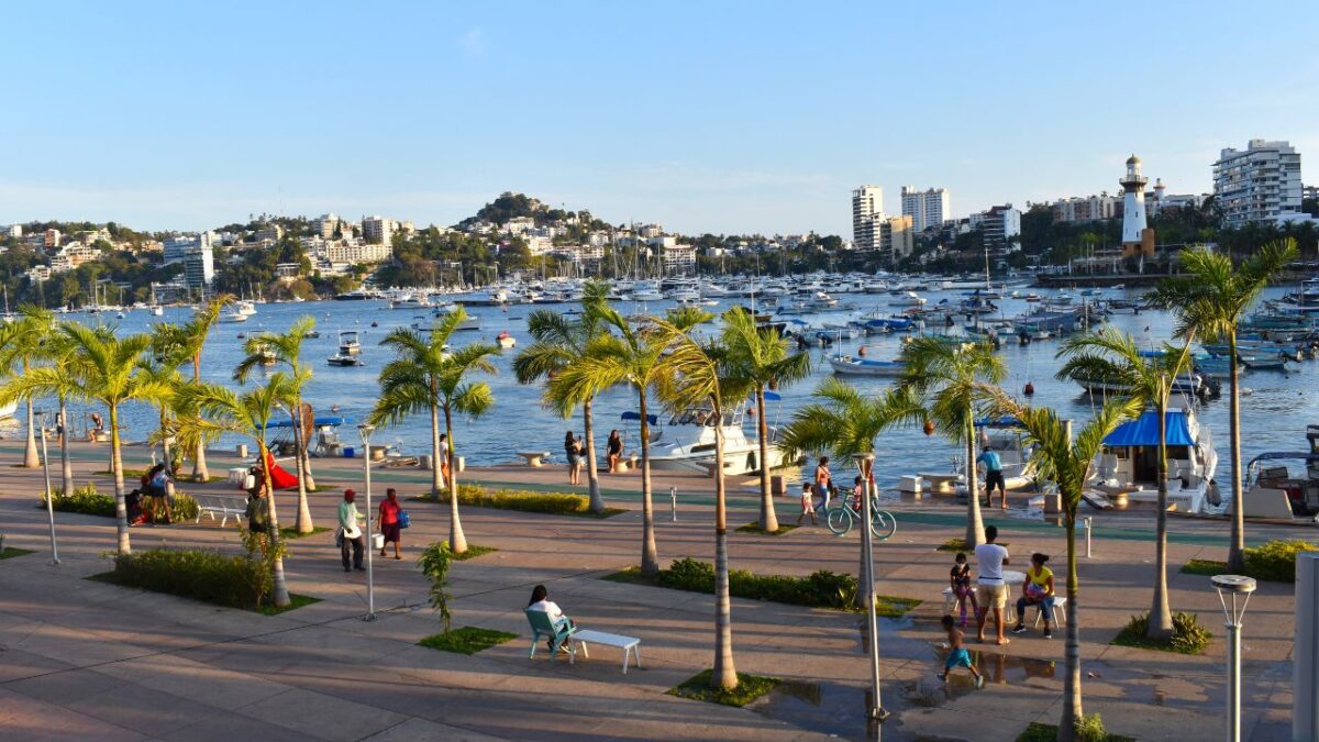 15 Nostalgic Travel Destinations for Anyone Who Grew Up in the '70s 8 People walk along a palm-lined promenade by a bay with boats, under a clear blue sky.