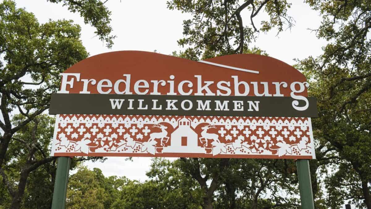 A “Fredericksburg Willkommen” sign with a red and white design stands among trees.