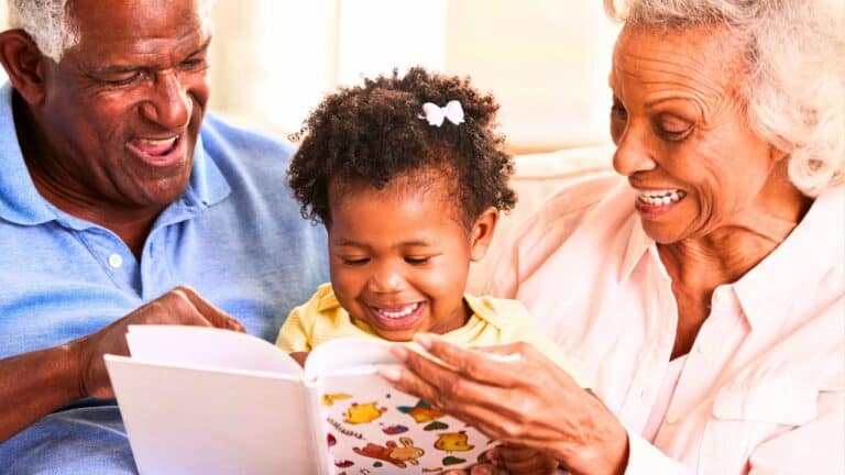 Smiling elderly couple and a young child reading a storybook together on a cozy couch.