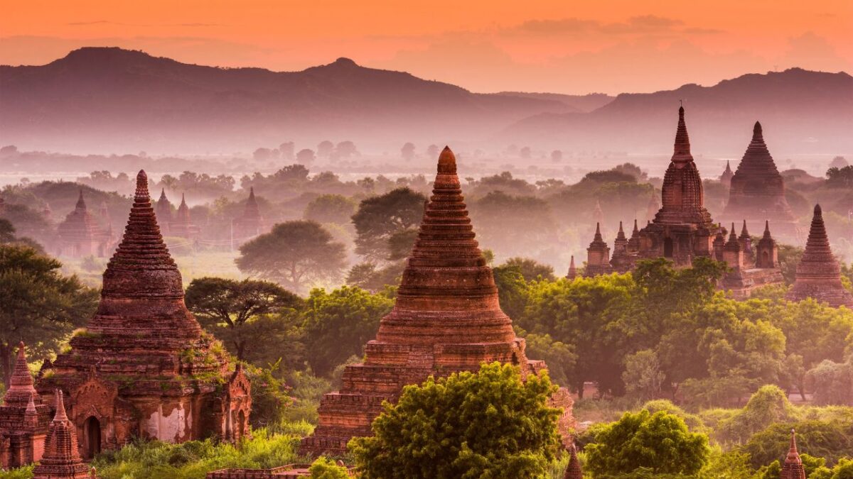 15 Nostalgic Travel Destinations for Anyone Who Grew Up in the '70s 5 Ancient temples and pagodas rise among trees at sunset in Bagan, Myanmar, with mist and hills in the background.