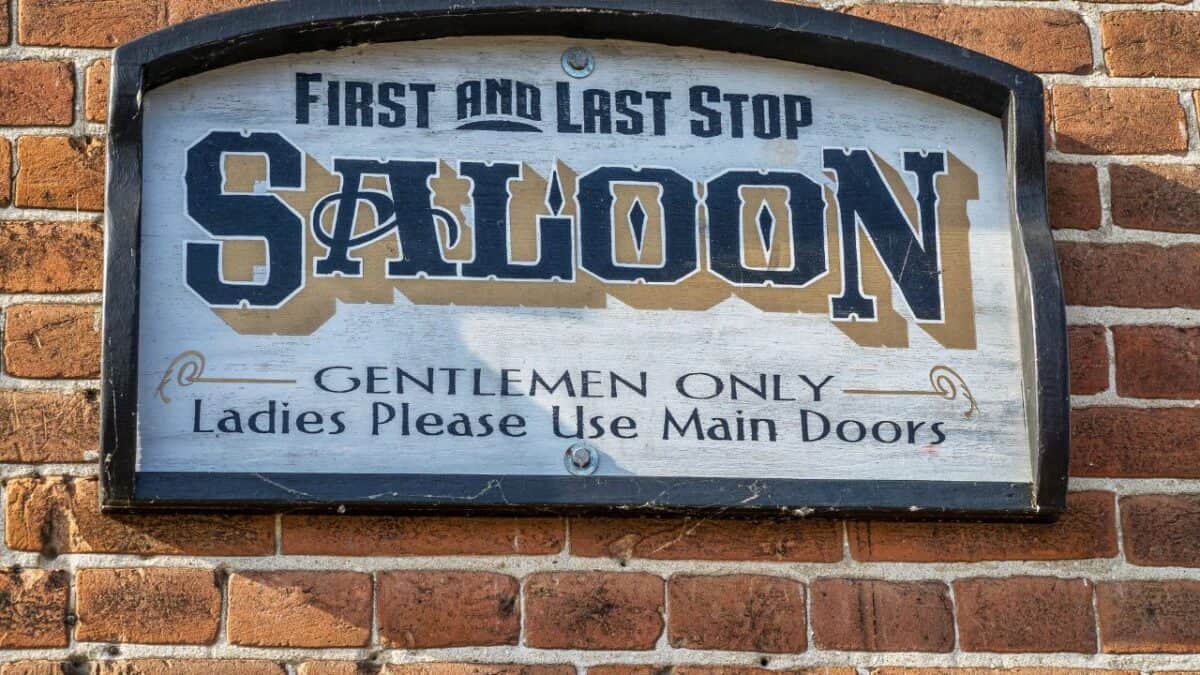 Sign reading: “Saloon Gentlemen only, ladies please use main doors,” on a brick wall.