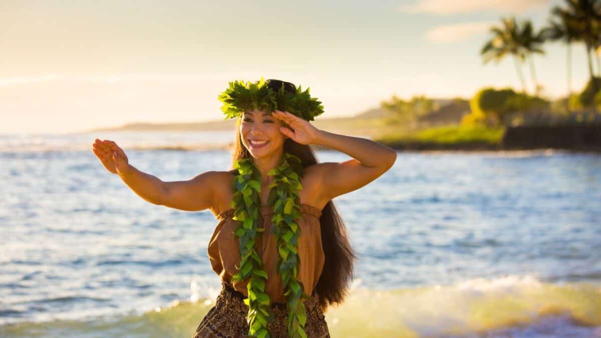 15 Nostalgic Travel Destinations for Anyone Who Grew Up in the '70s 7 Woman in traditional Hawaiian attire dancing hula on a beach at sunset, with palm trees in the background.