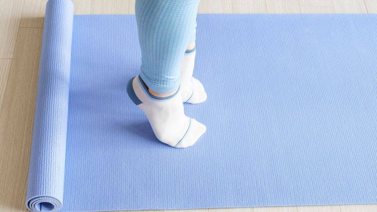 Person standing on a blue yoga mat with rolled edge, wearing light blue leggings and white socks.