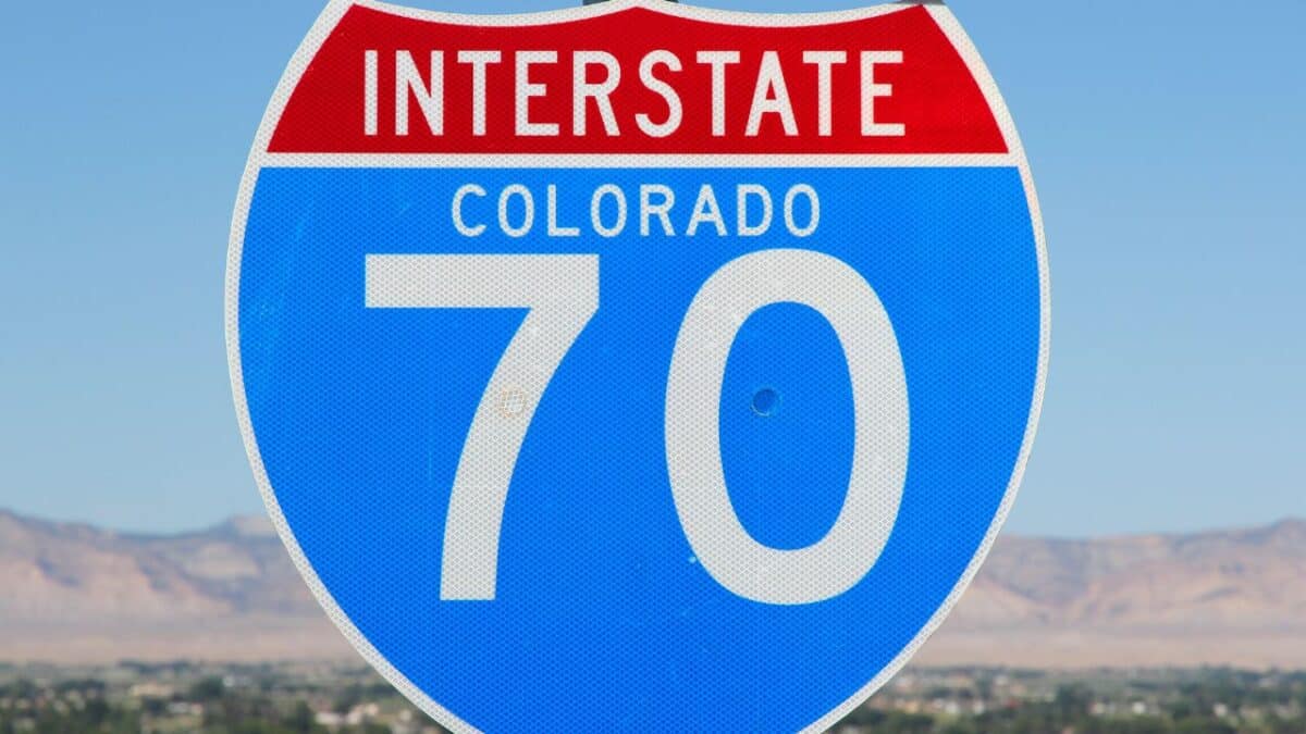 Close-up of an Interstate 70 sign marked with 'Colorado' against a clear blue sky and a distant view of a desert landscape with mountains.