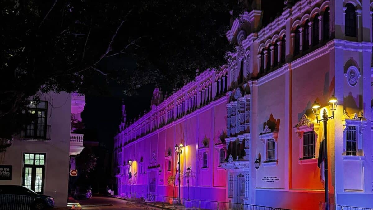 A historic building at night is lit up with purple, blue, and pink lights along its ornate facade.
